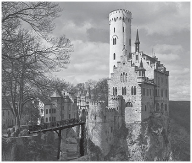 Fotografia em preto e branco de um castelo sobre um penhasco rochoso. O castelo tem uma torre cilíndrica alta e várias torres menores. Uma ponte estreita e elevada se estende do castelo para a esquerda, ligando-o a outras construções.
