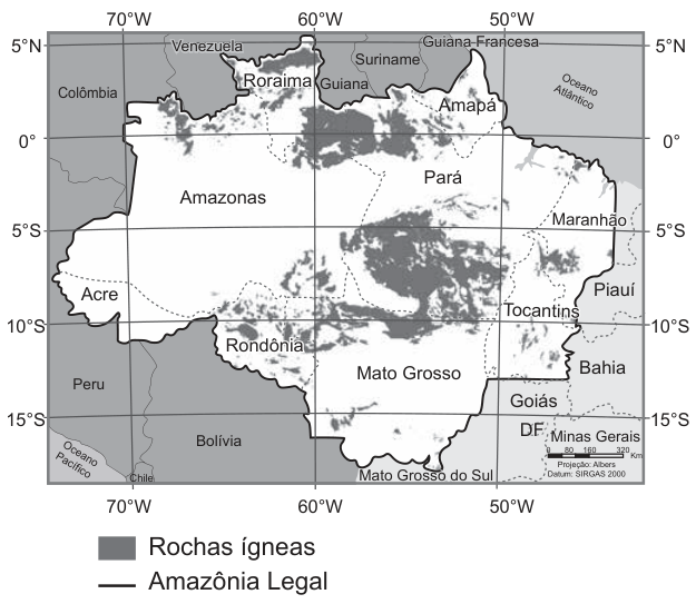 Mapa da Amazônia Legal, com estados e coordenadas de 70° a 50° oeste e de 5° norte a 15° sul. O contorno preto delimita a Amazônia Legal; manchas cinzas indicam rochas ígneas. As maiores concentrações aparecem no norte, entre Roraima, norte do Pará e Amapá, e no sul do Pará, estendendo-se pelo norte de Mato Grosso. Há manchas menores em outras áreas.