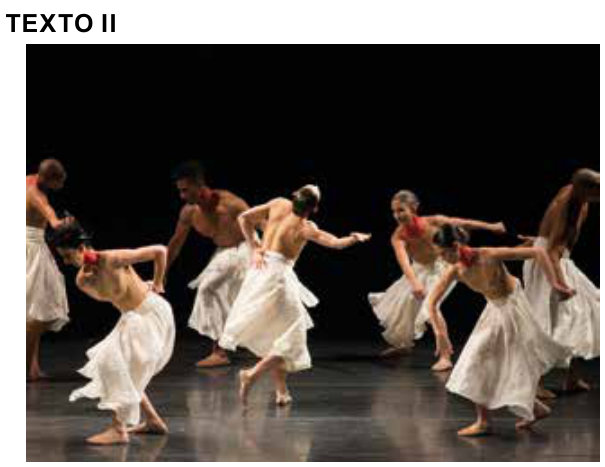 Fotografia de um espetáculo de dança em um palco de fundo preto. Sete bailarinos descalços usam saias brancas rodadas; alguns estão de torso nu, outros vestem blusas em tons próximos ao da pele. Com os corpos inclinados ou girando, estendem os braços em diferentes direções.